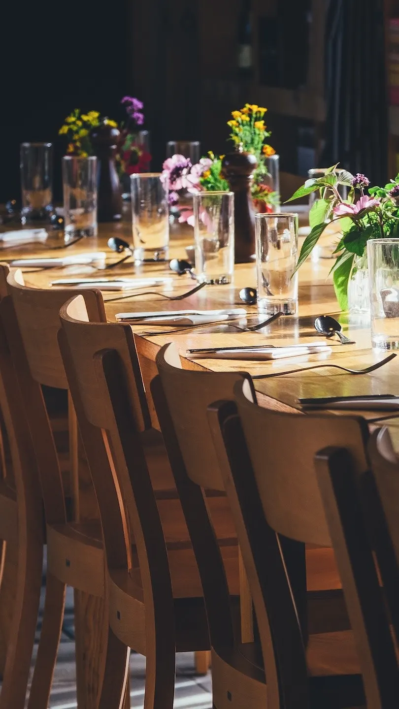 Grande table en bois dressée, chaises alignées et bouquets de fleurs des champs