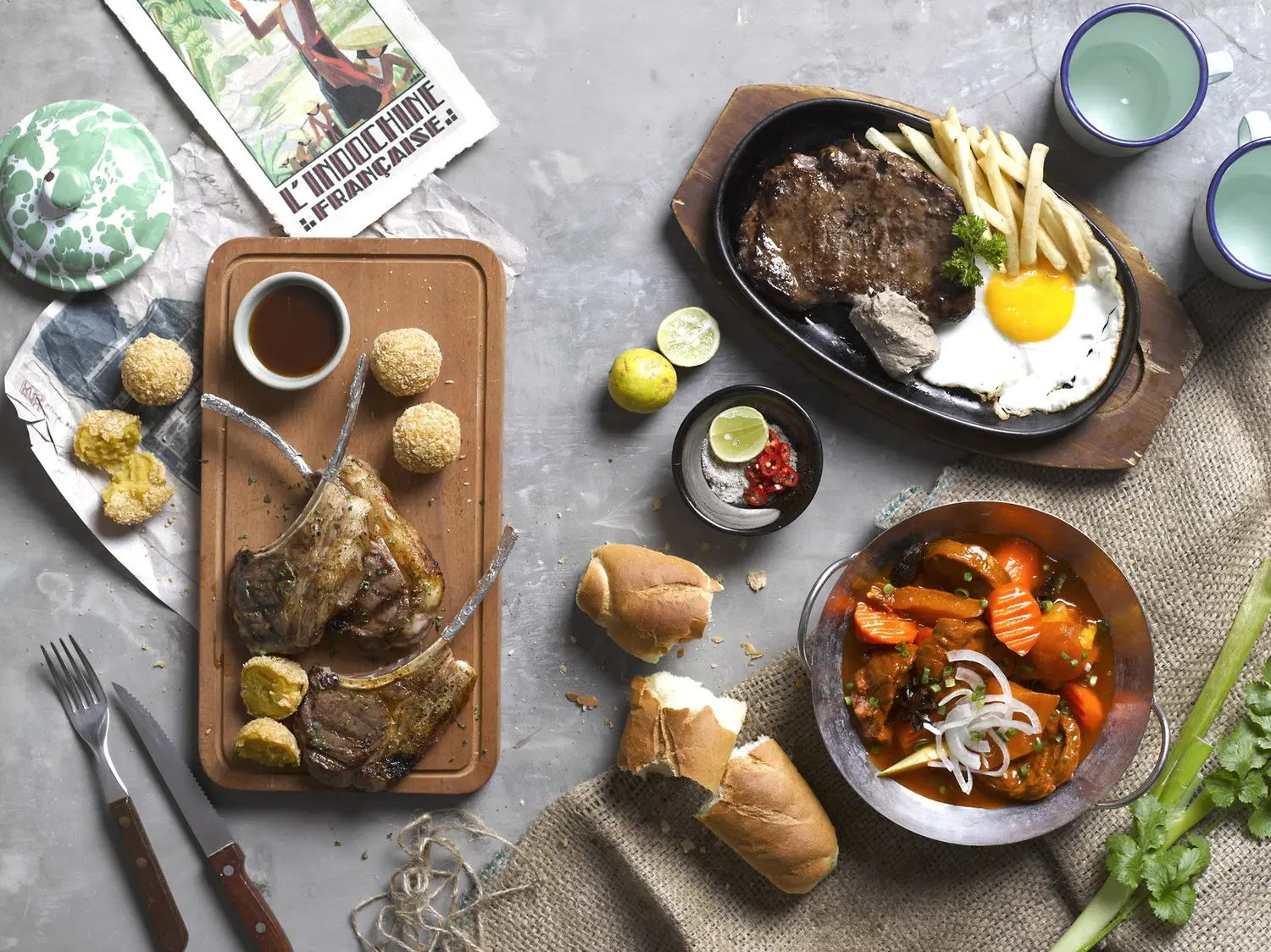 Plusieurs plats posés côte à côte sur une table : côtelettes, ragoût, pain et condiments