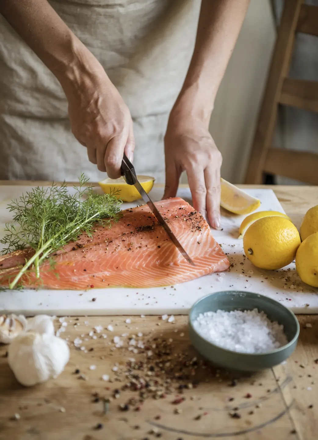 Deux mains tranchant un filet de saumon à l’aneth sur une planche de marbre